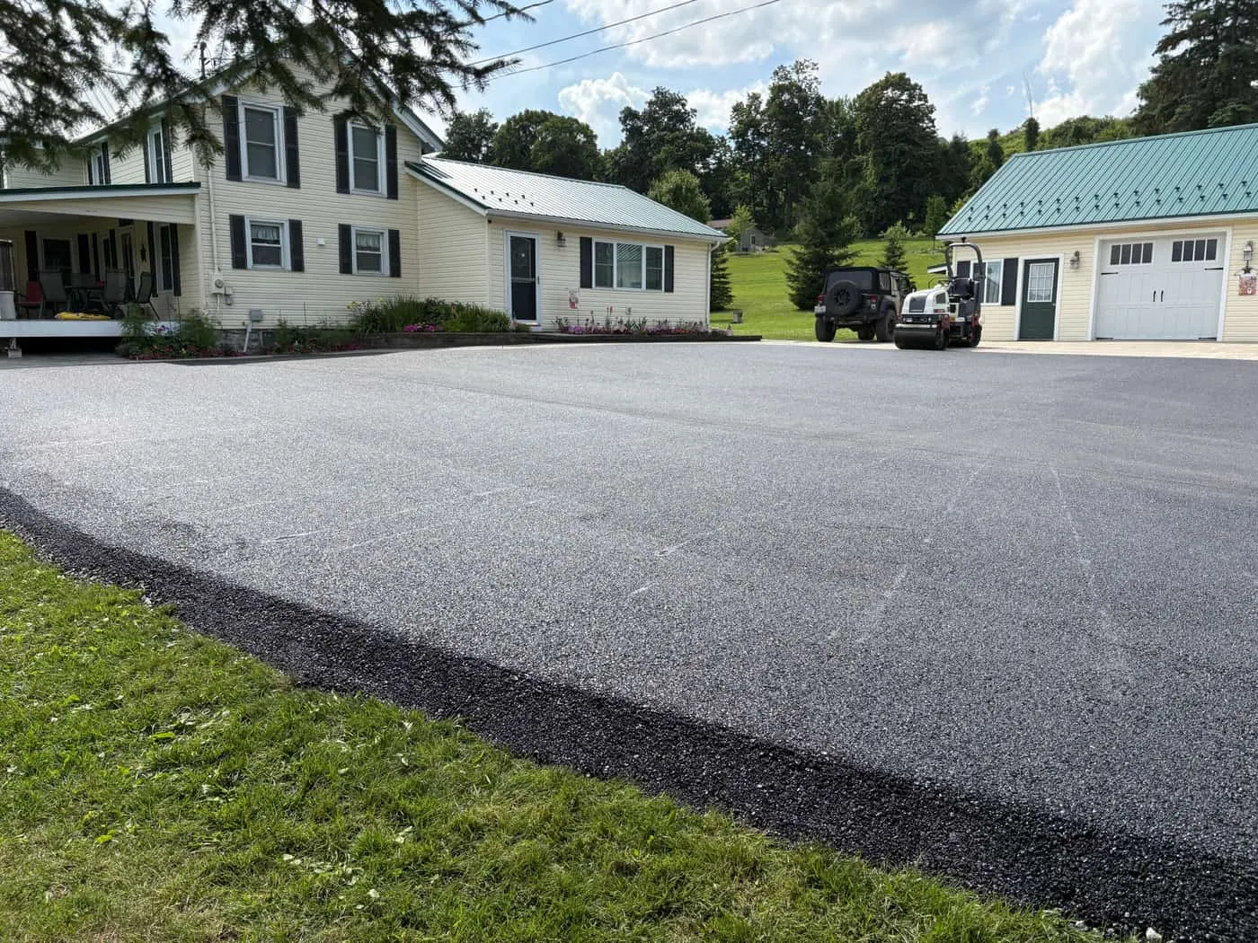 A spacious freshly paved asphalt driveway leading toward a garage and home on a sunny day.